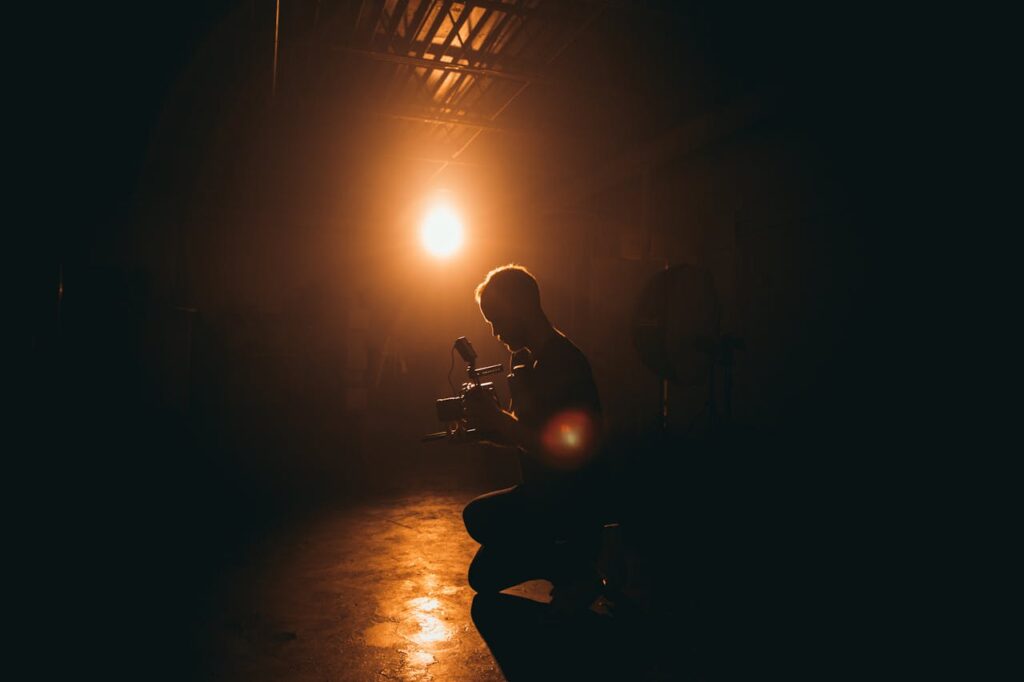 pexels-photo-3379942 Silhouette of a cinematographer operating a camera in a dimly lit studio with dramatic lighting.